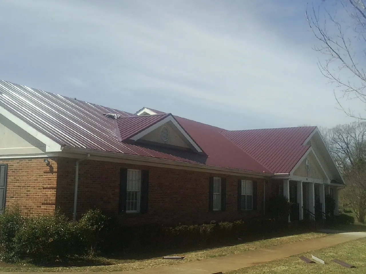 Red metal roof with gabled entries on a long brick building, from a Hail Damage Roof Repair job in Pierre Part