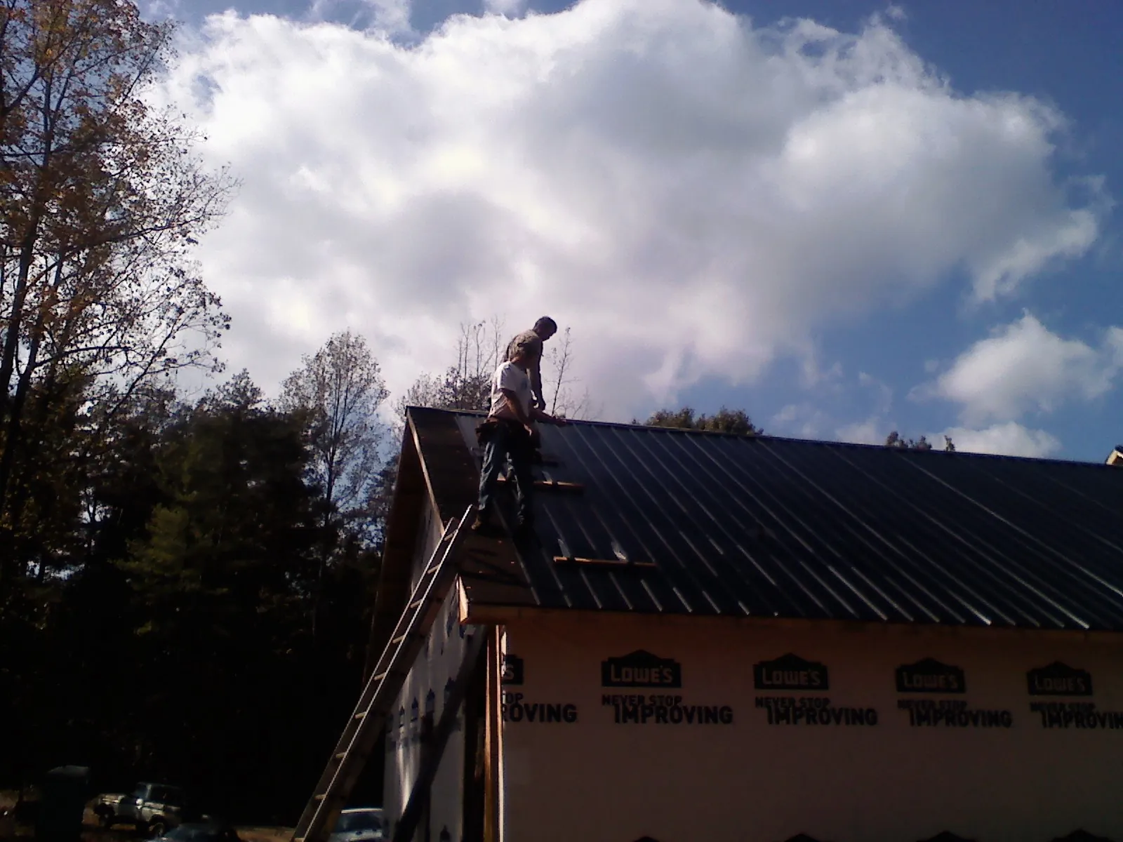 Roofer fastening dark metal panels high against a cloudy sky, from a Roof Inspection job in Pierre Part
