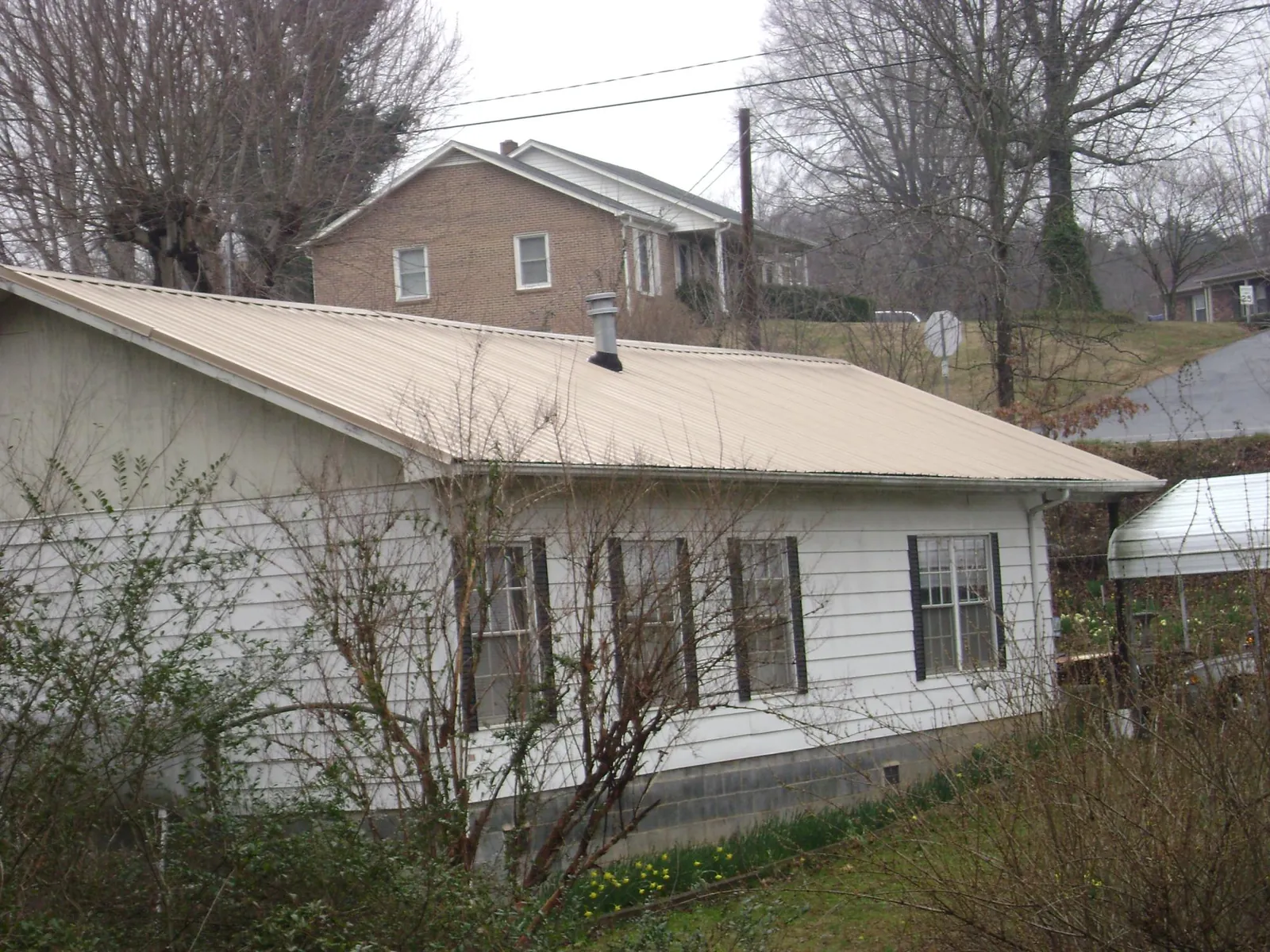 Tan metal roof on a white sided house set into a hillside — Commercial Roofing by Roofing Brothers in Pierre Part