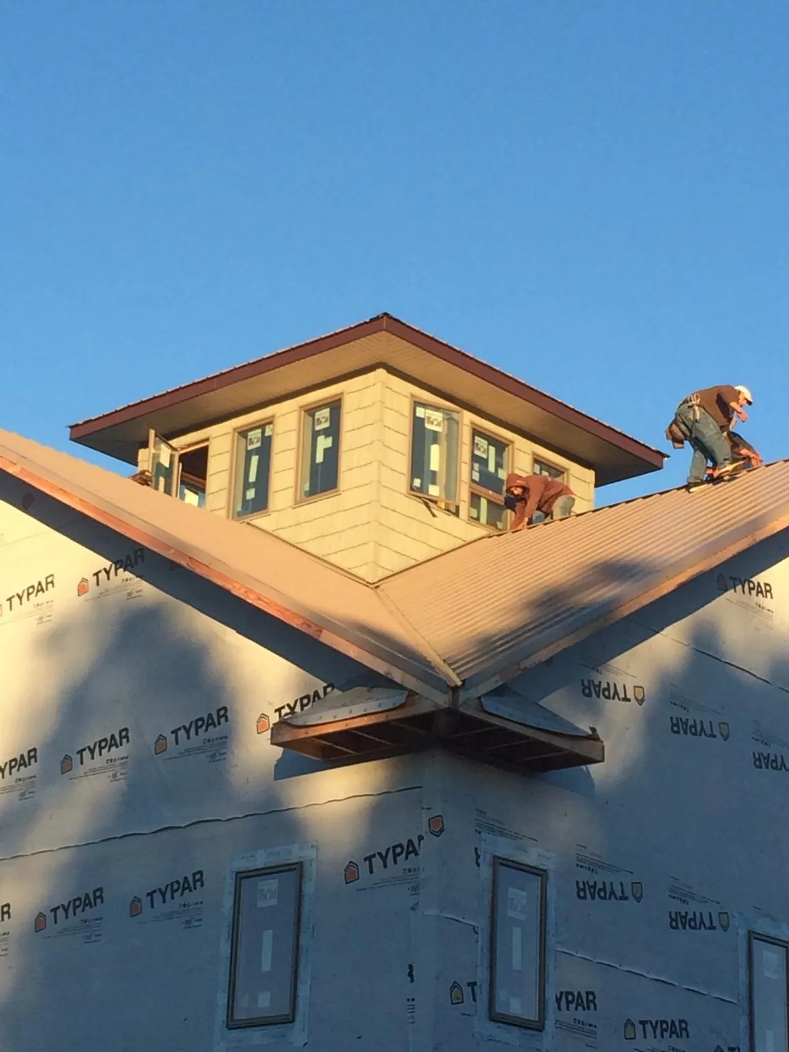 Roofers working around a rooftop cupola on a new metal roof at sunset — Roof Waterproofing in Pierre Part by Roofing Brothers
